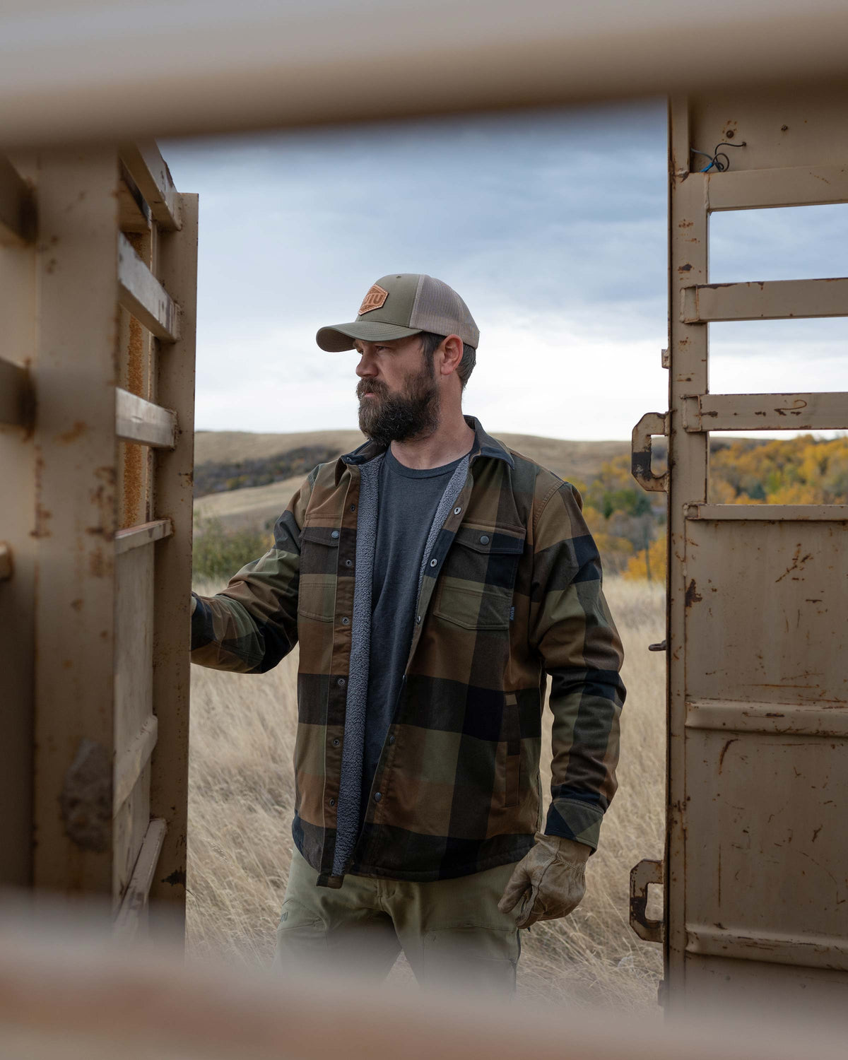 Hunter looking away, closing the door on the cattle trailer, wearing Field Flannel Shirt in Valo Plaid 