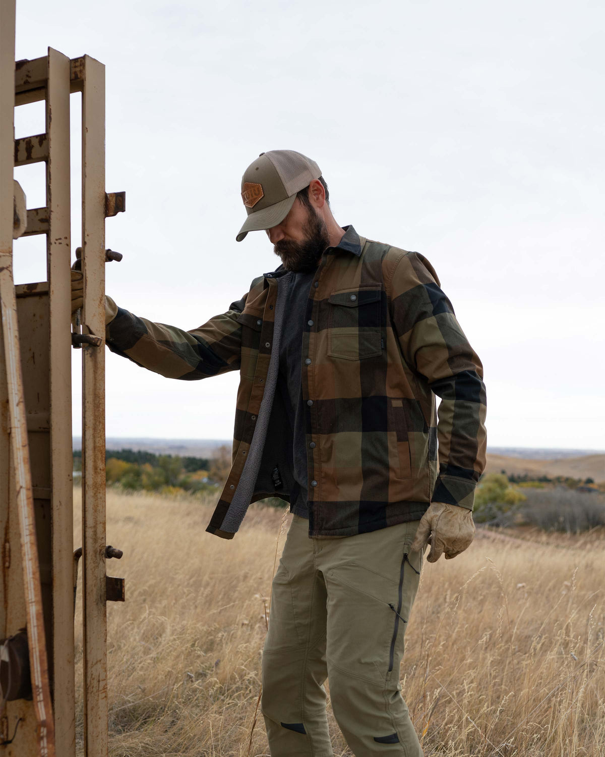 Hunter looking down, carefully closing the door on the cattle trailer, wearing Field Flannel Shirt Jacket in Valo Plaid