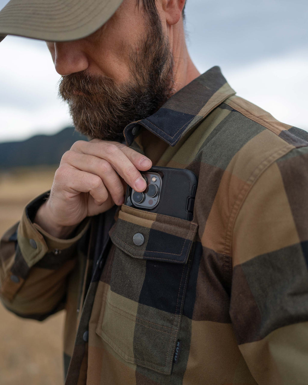 Hunter slipping a cellphone in his front left chest pocket on the Field Flannel Shirt Jacket in Valo Plaid