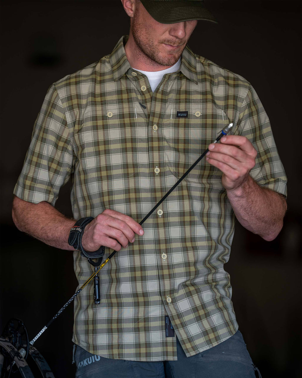 Man wearing Borrego Short Sleeve Shirt in Valo Crosscheck Plaid while accessing the tip of an arrow.