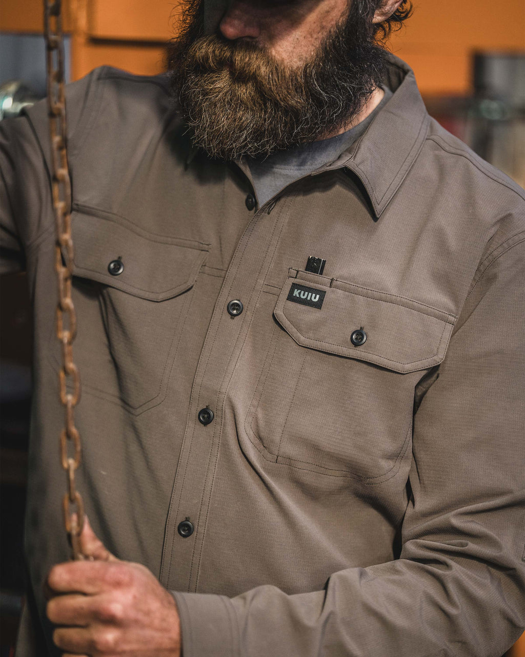 Close-up of man gripping a hanging metal chain wearing Gauge Long Sleeve Work Shirt in Rodeo Brown.