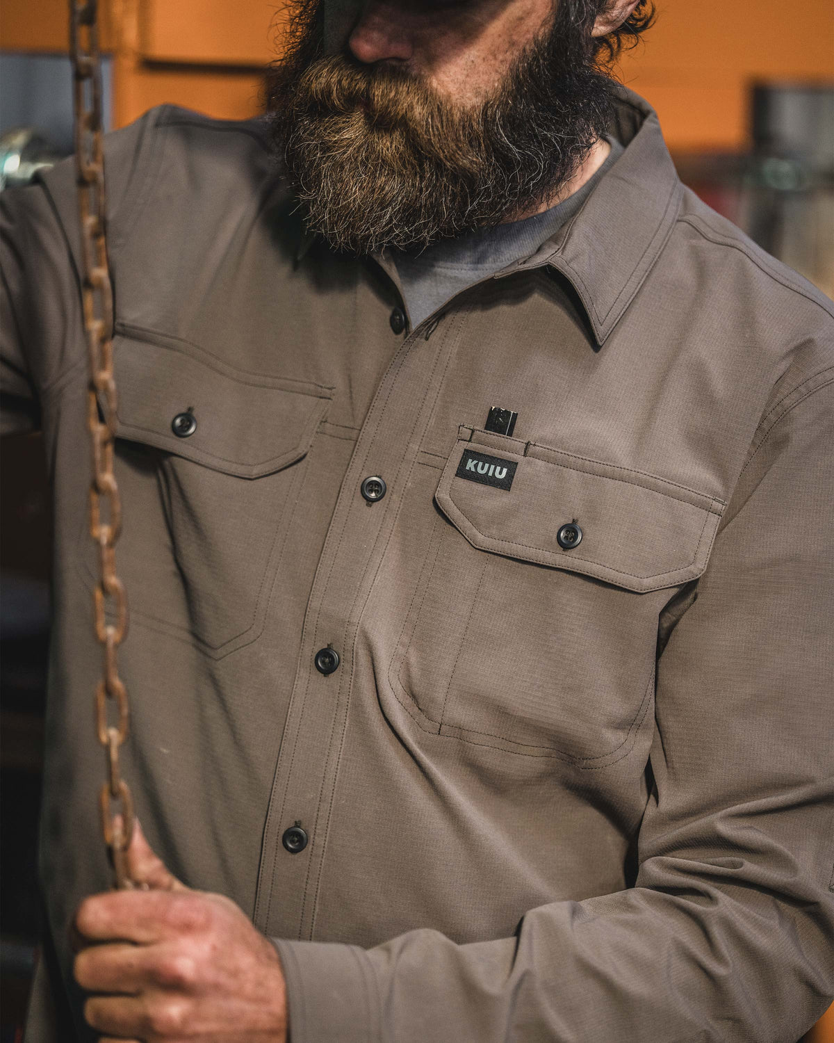 Close-up of man gripping a hanging metal chain wearing Gauge Long Sleeve Work Shirt in Rodeo Brown.