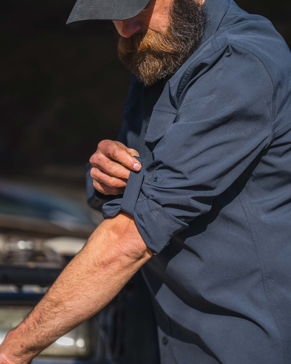 Man wearing Gauge Long Sleeve Shirt in Nightfall Blue, displaying rollable sleeve with snap-closure tabs on the Gauge Long Sleeve Work Shirt in Nightfall Blue.