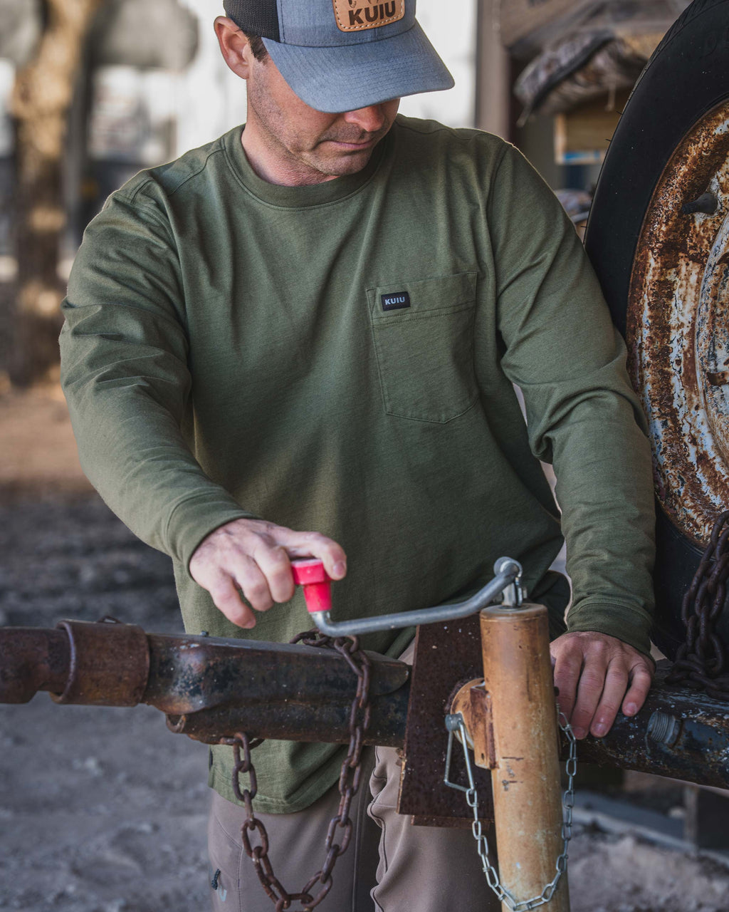 Man standing next to a heavy metal equipment, griping a red‑handled metal crank, wearing Workgrade Long Sleeve Pocket Crew in Evergreen.