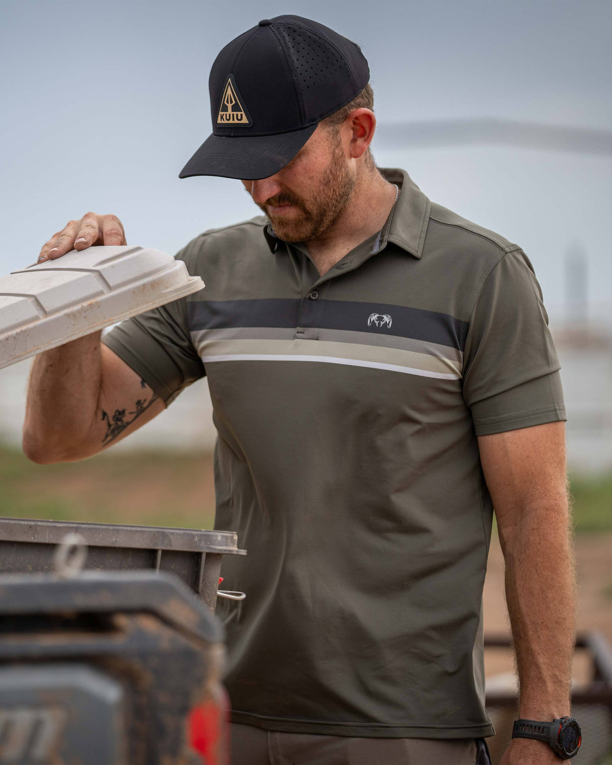 Man lifts storage chest lid and appears to look inside wearing KUIU Performance Polo Chest Stripe in Ash Stripe
