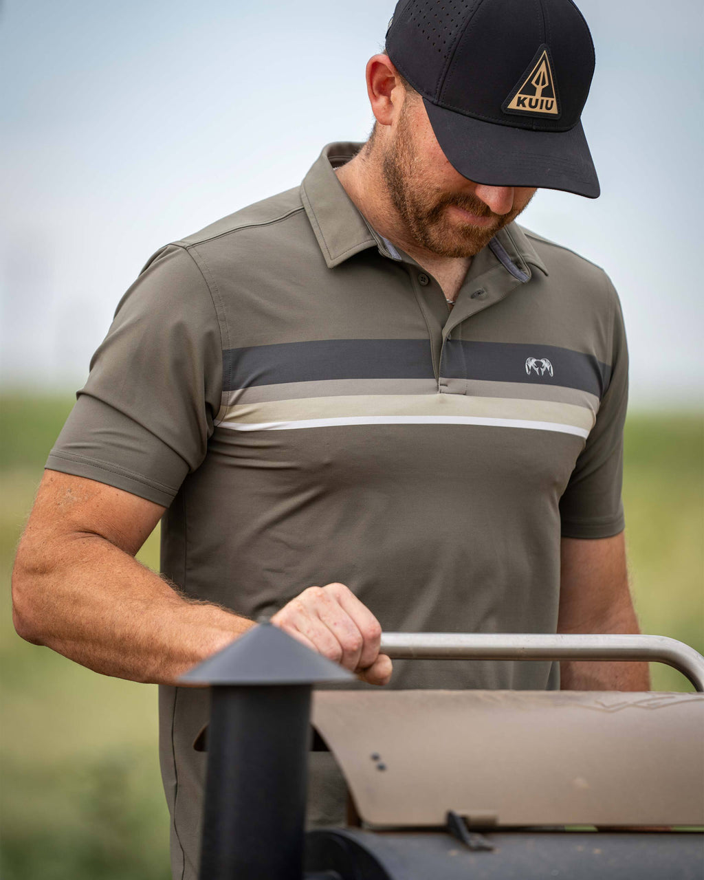 Man gripping onto a barbeque grill handle wearing KUIU Performance Polo Chest Stripe in Ash Stripe