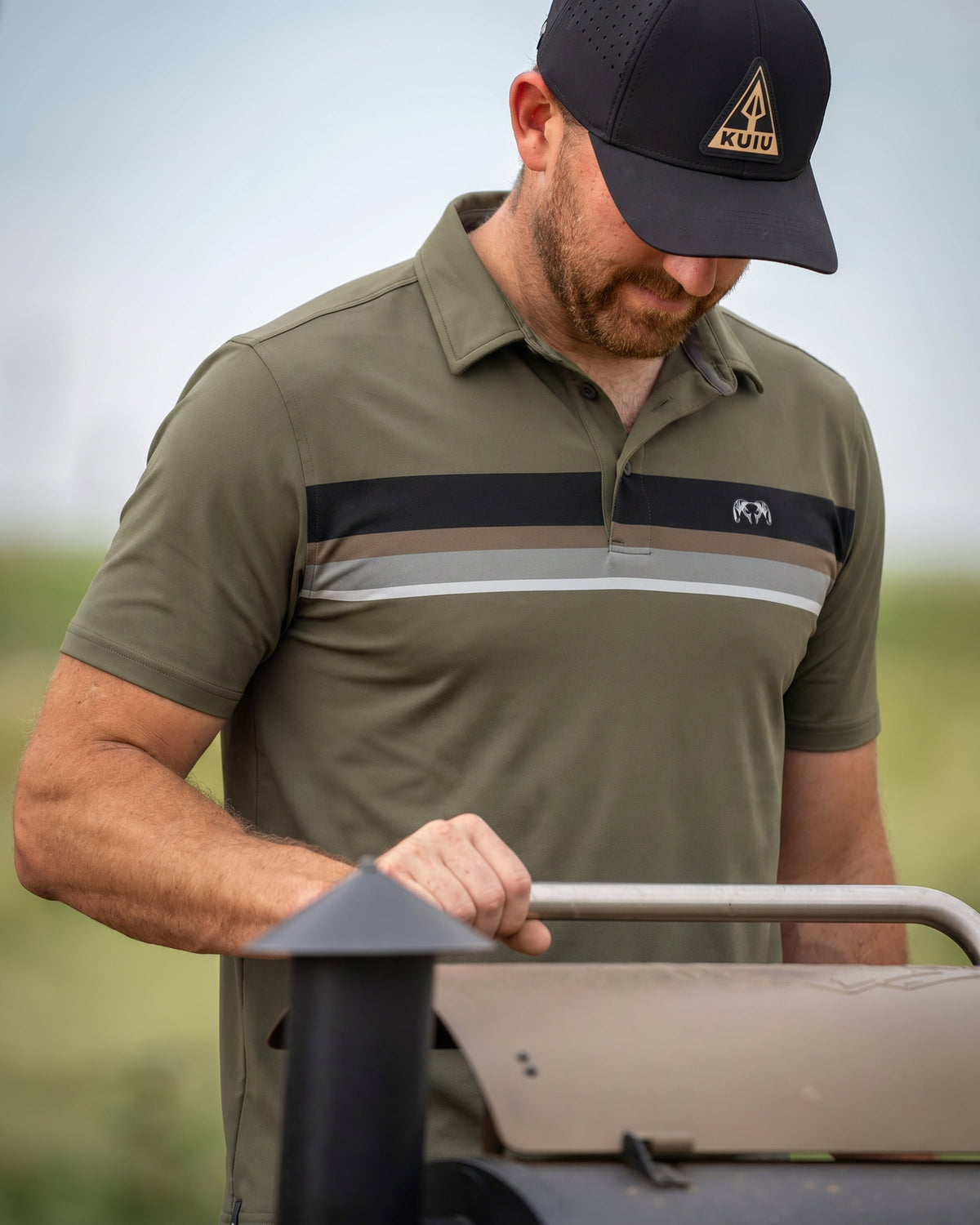 Man gripping onto a barbeque grill handle wearing KUIU Performance Polo Chest Stripe in Evergreen Chest Stripe