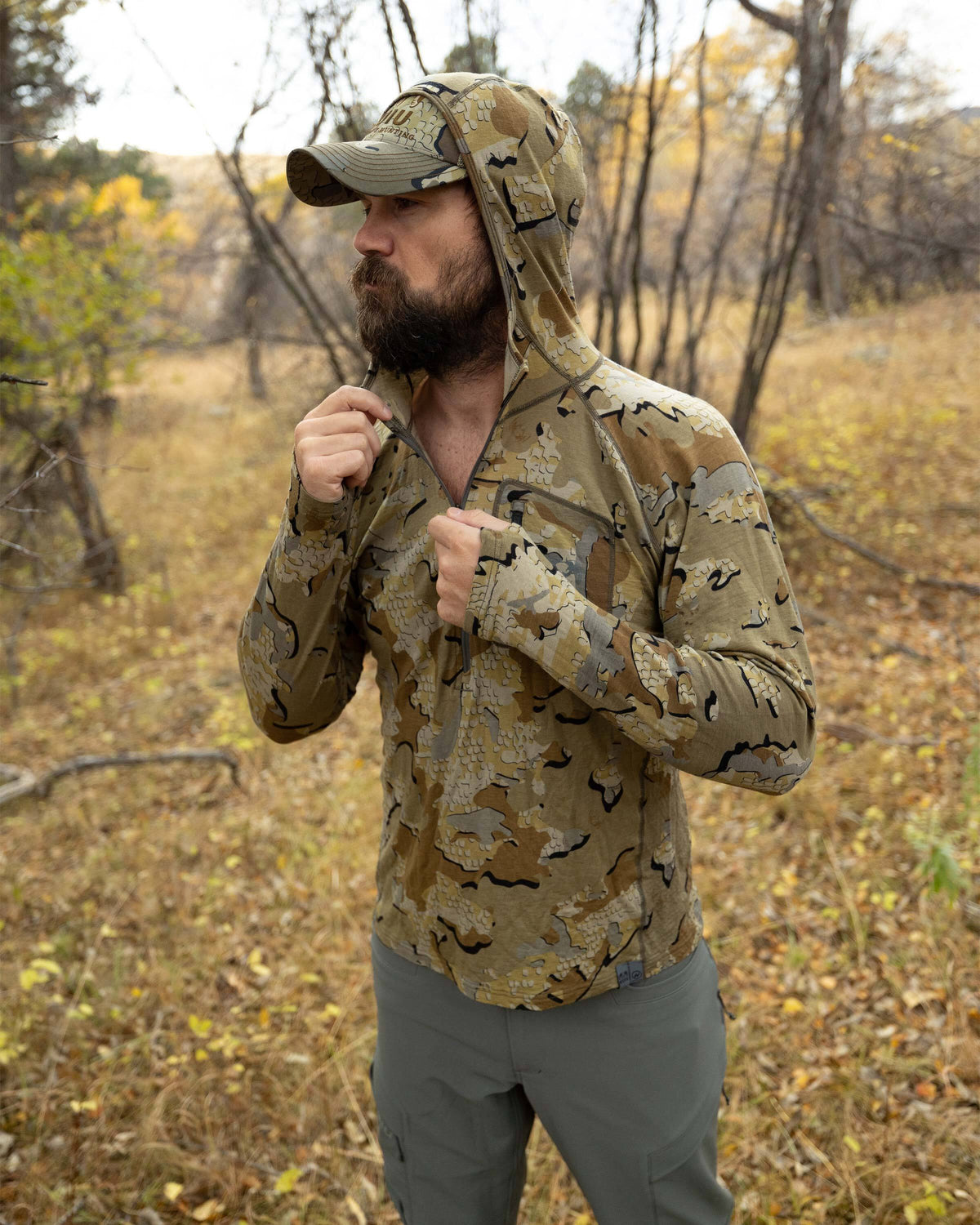 Hunter standing in the middle of the wood, zipping up his Ultra Merino 145 Zip-T Hunting Hoodie in Valo Camouflage with hood over his head 