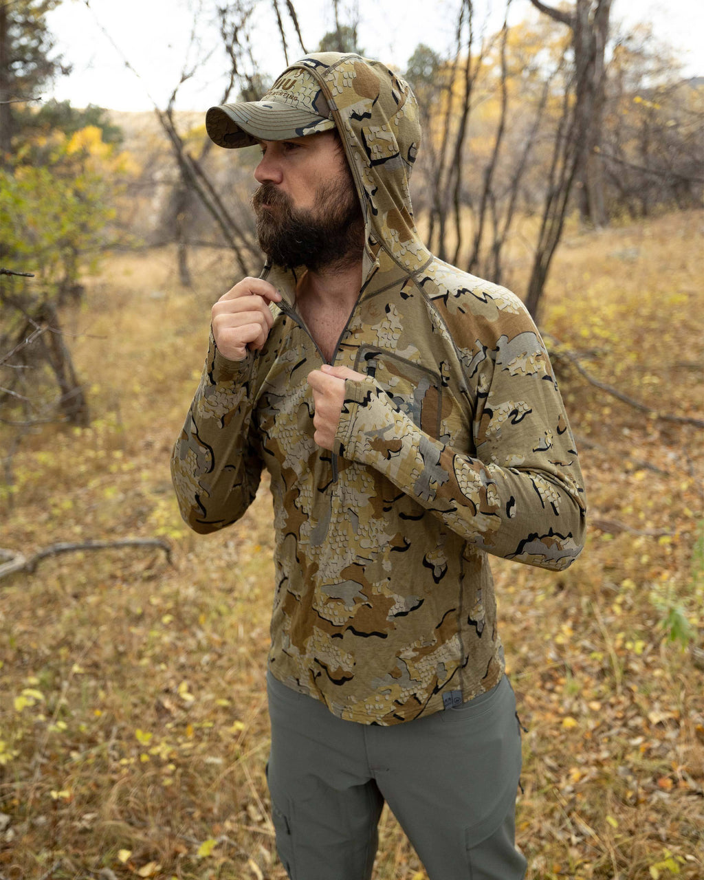 Hunter standing in the middle of the wood, zipping up his Ultra Merino 145 Zip-T Hunting Hoodie in Valo Camouflage with hood over his head 