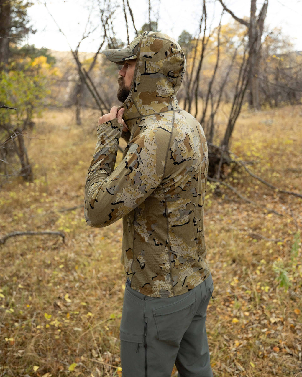 Side profile of Hunter adjusting the hood on this ULTRA Merino 145 Zip-T Hoodie in Valo Camouflage