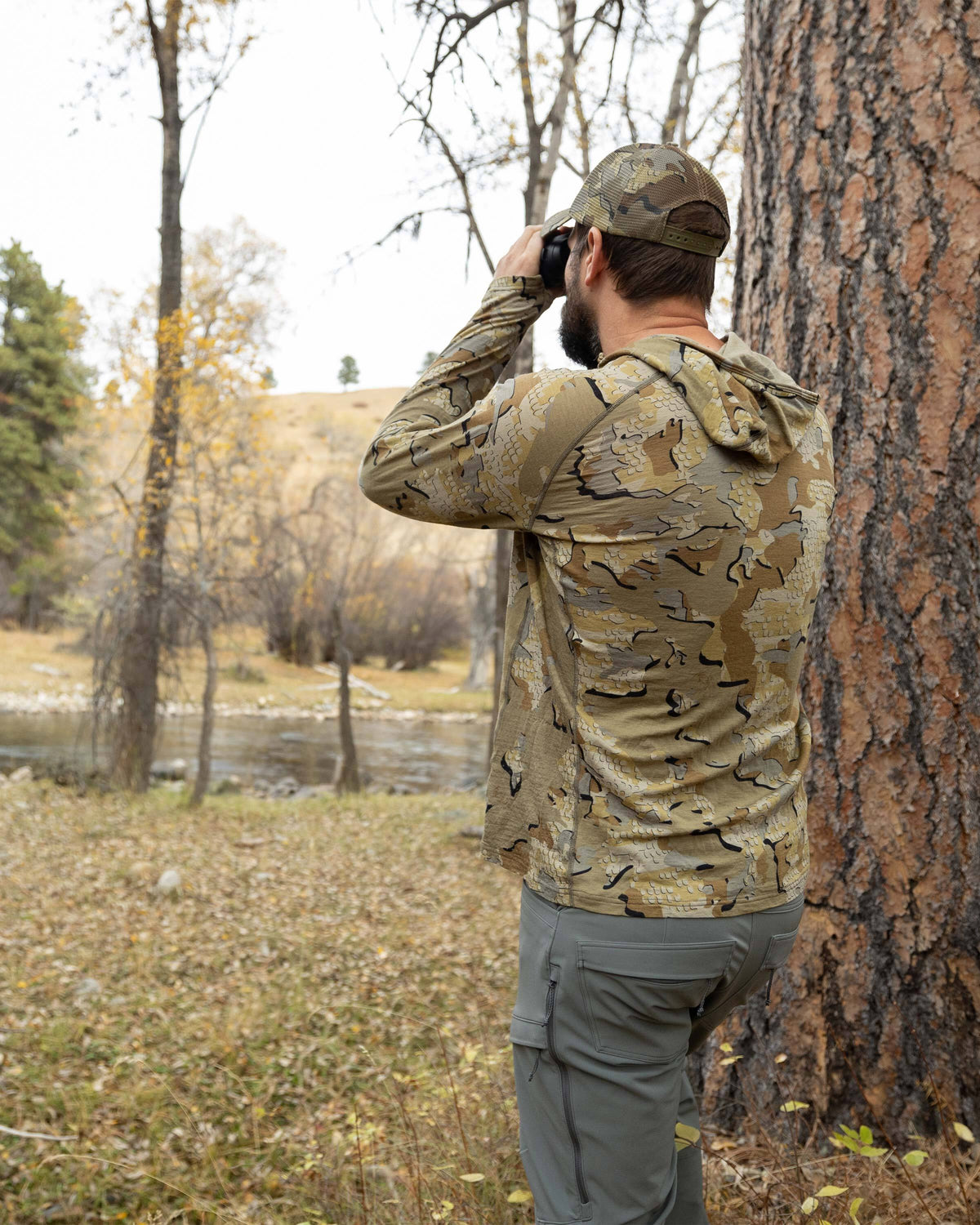 Back view of Hunter in the wood glassing, wearing ULTRA Merino 145 Zip-T Hunting Hoodie in Valo Camouflage