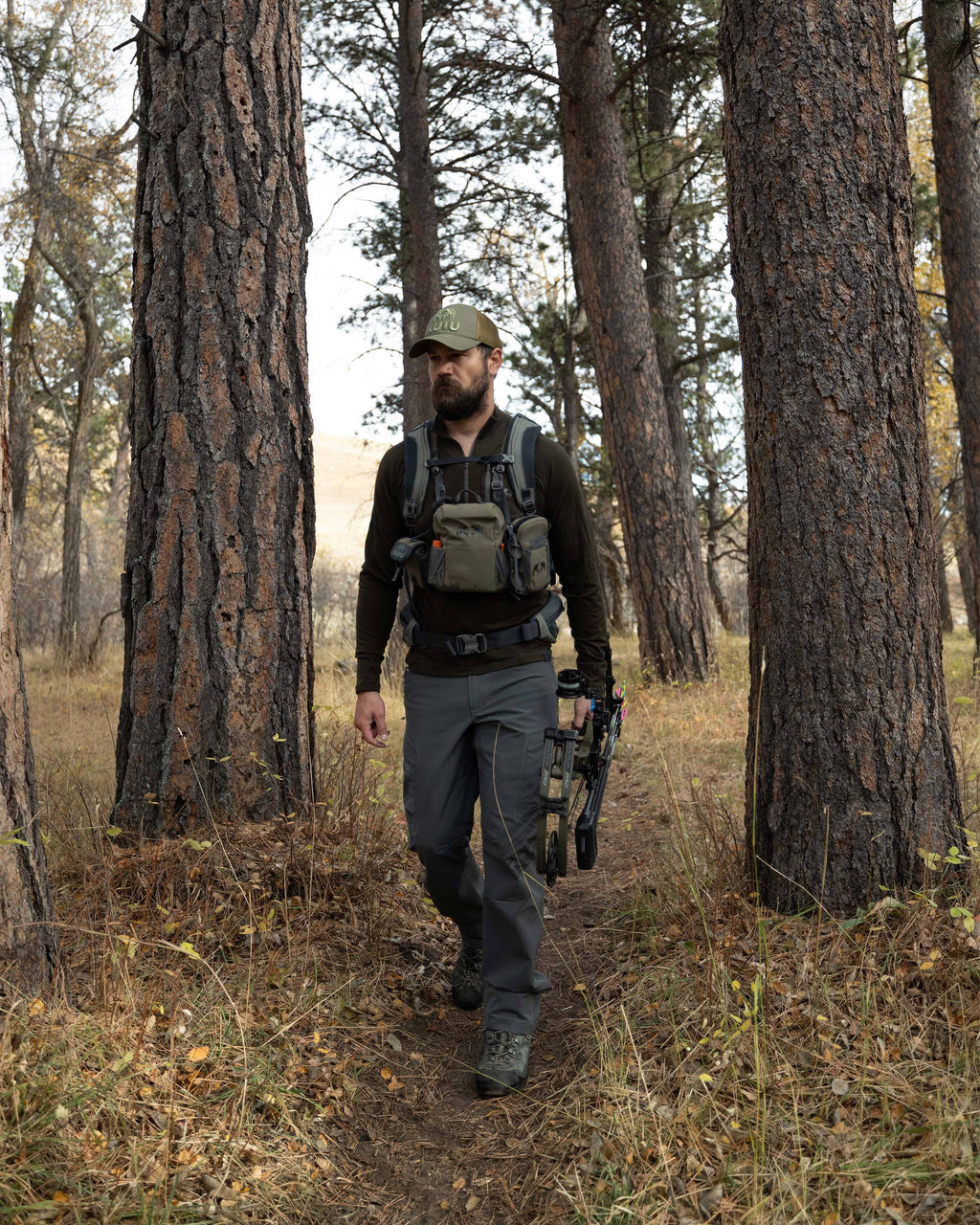 Hunter walking through the forest, holding his bow, wearing Ultra Merino 145 Zip-T Hunting Shirt