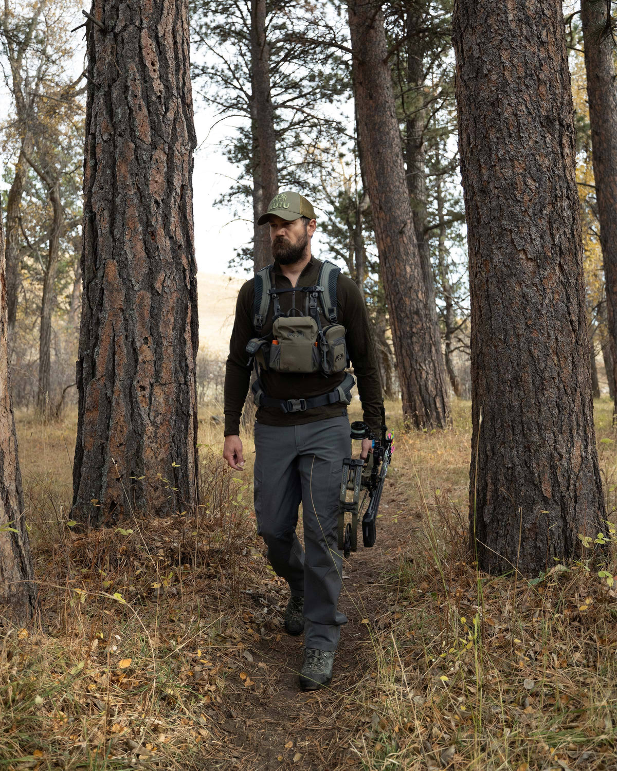 Hunter walking through the forest, holding his bow, wearing Ultra Merino 145 Zip-T Hunting Shirt