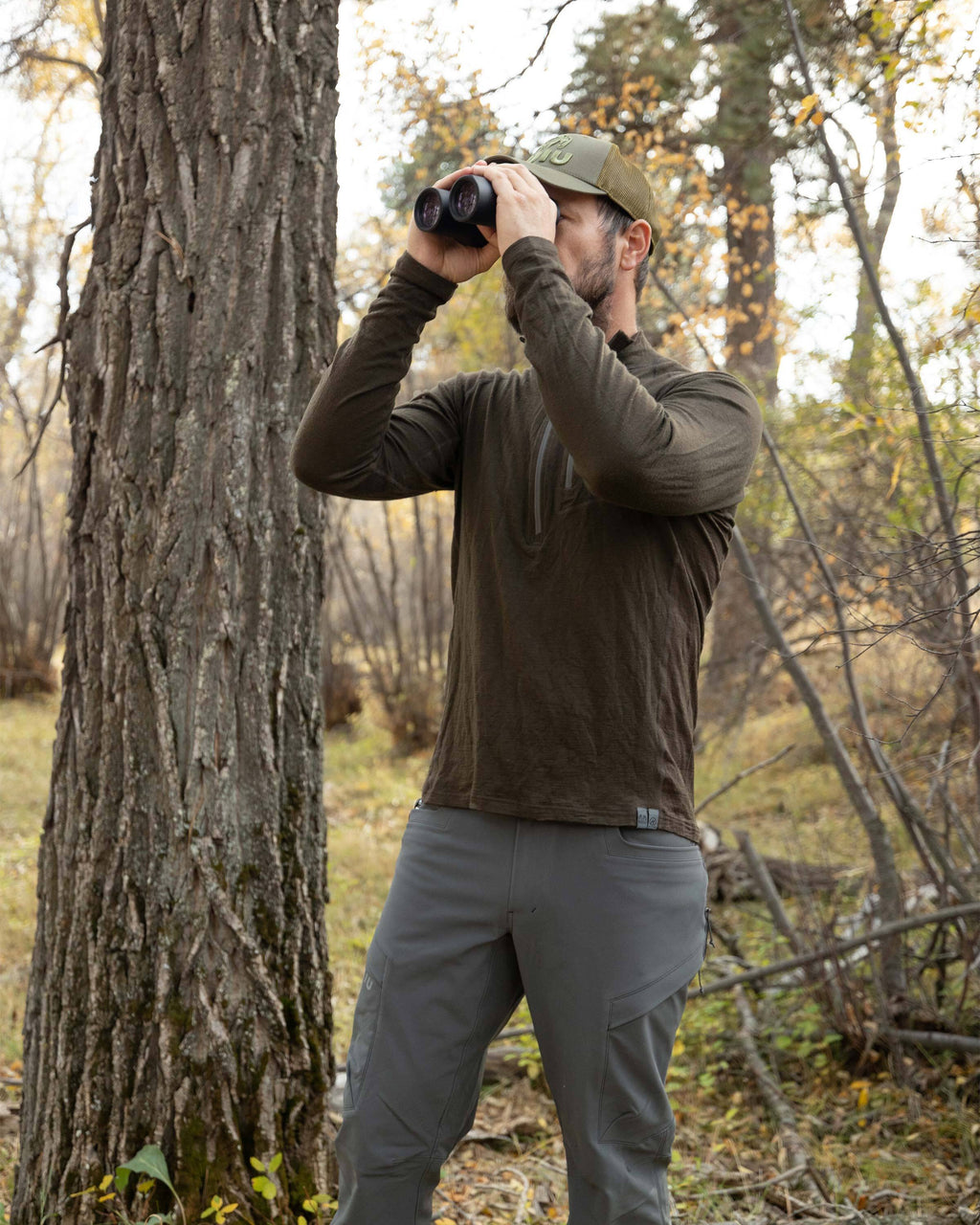 Hunter standing in the woods, glassing, wearing ULTRA Merino 145 Zip-T Hunting Shirt in Loden Green