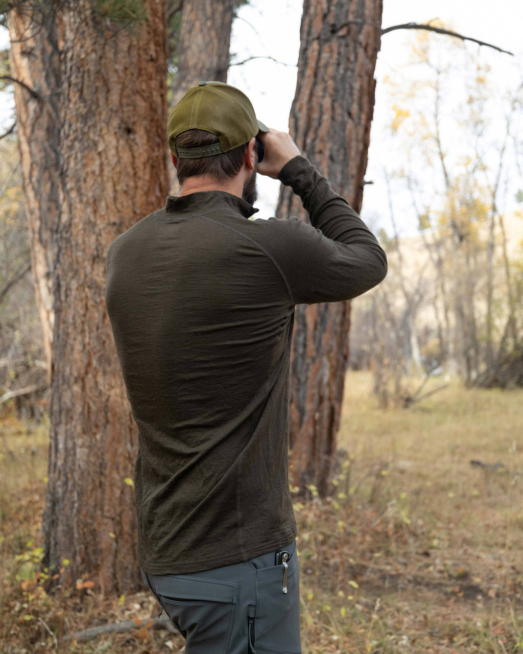 Back view of Hunter in the wood glassing, wearing Ultra Merino 145 Zip-T Hunting Shirt Loden Green