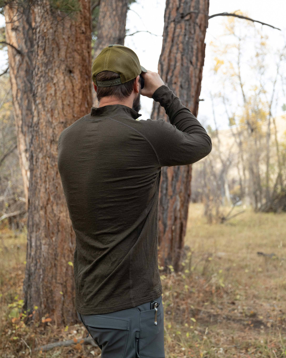Back view of Hunter in the wood glassing, wearing Ultra Merino 145 Zip-T Hunting Shirt Loden Green