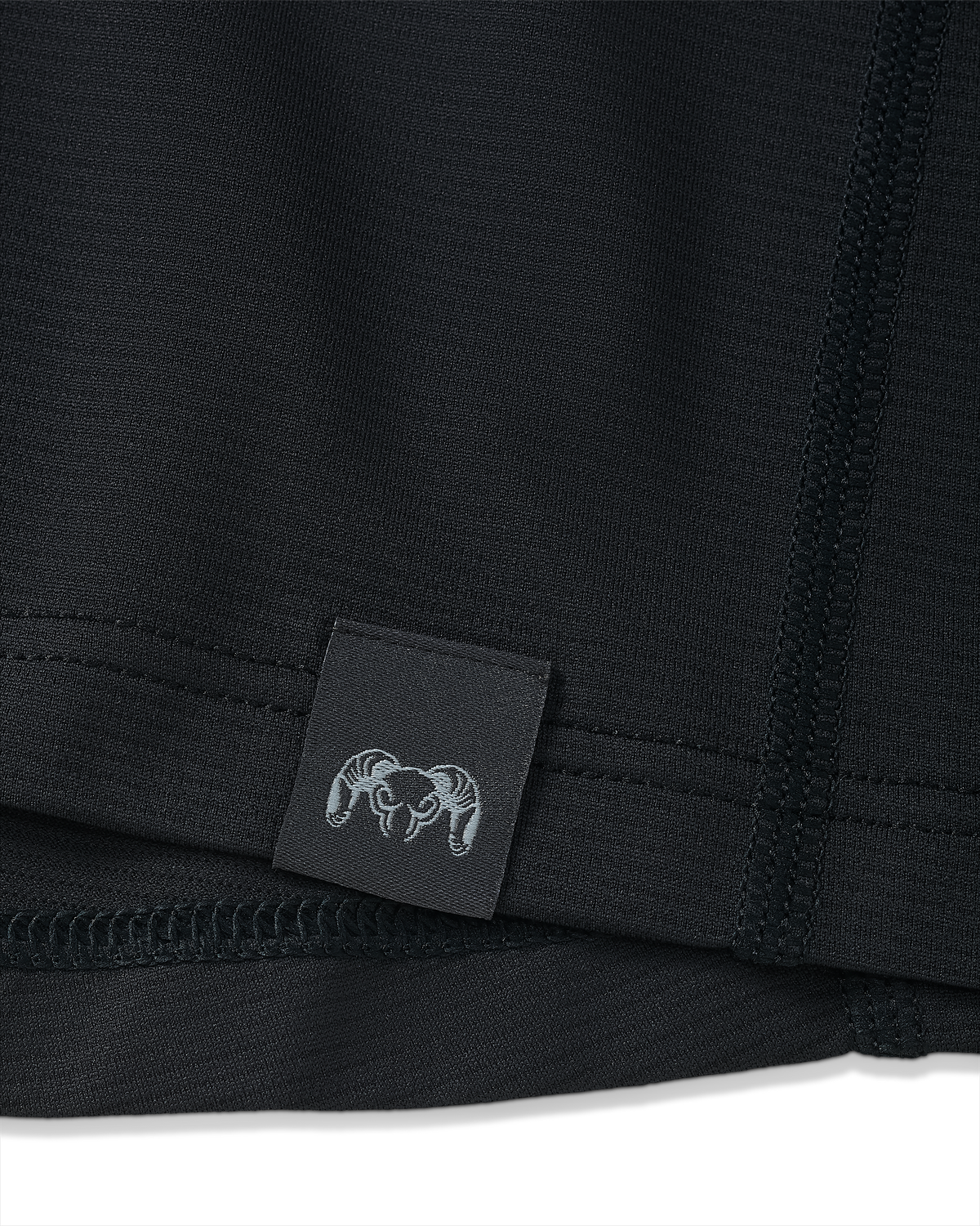 Close-up view of bottom seam of Vital S1 Short Sleeve in Black, Displaying a sewn in KUIU Ram logo on sewn-in tag 