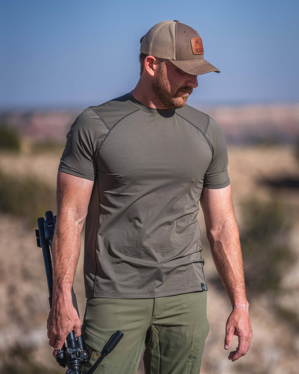 Hunter wearing Vital S1 Short Sleeve Crew in Ash Brown, standing in an outdoor environment, holding a tripod.