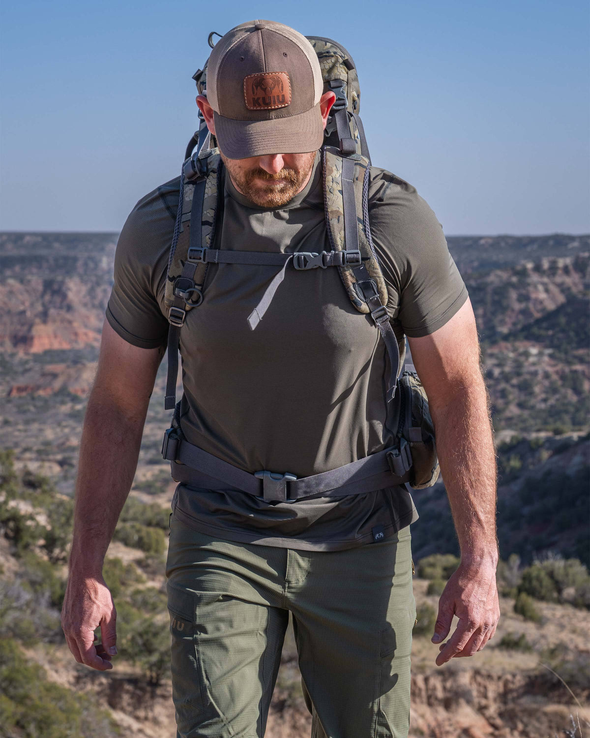 Hunter backpacking in an open landscape with a scenic layered canyon walls, wearing Vital S1 Short Sleeve in Ash Brown