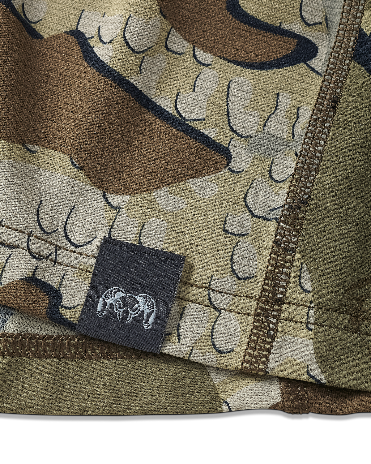 Close-up view of bottom seam of Vital S1 Short Sleeve in Valo Camouflage, Displaying a sewn in KUIU Ram logo on sewn-in tag 