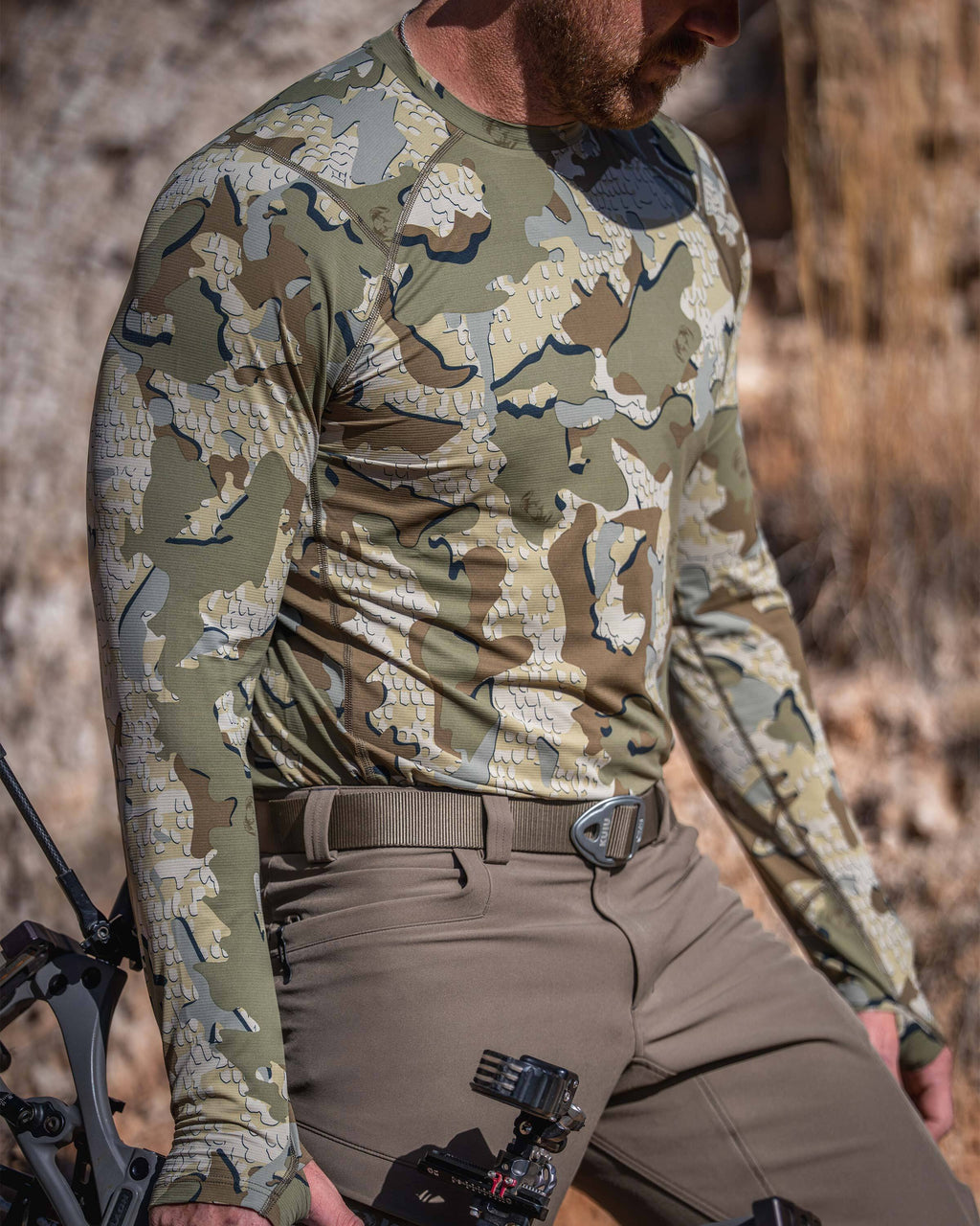 Hunter in an outdoor setting holding a compound bow, wearing Vital S1 Long Sleeve Crew in Valo Camouflage.