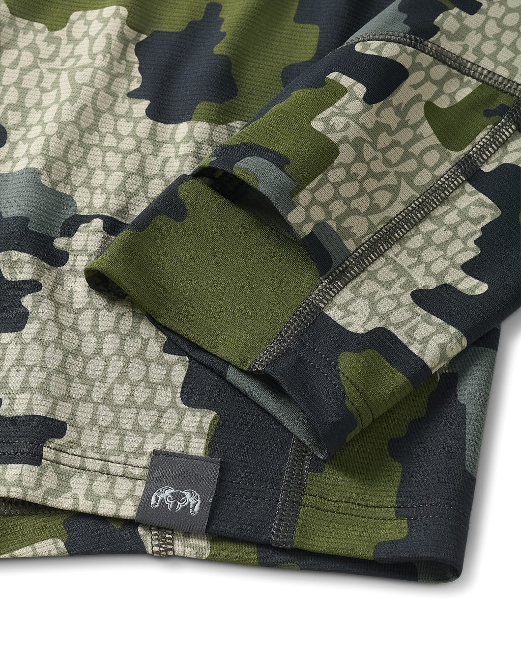 Close-up view of bottom seam of Vital S1 Short Sleeve in Verde Camouflage, Displaying a sewn in KUIU Ram logo on sewn-in tag 