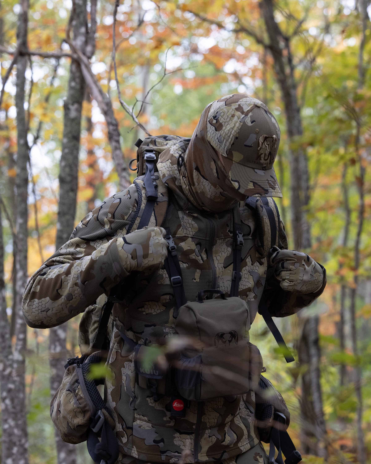 Hunter in the field wearing a Valo Camouflage Hat and the Peloton 240 Full Zip Hoodie in Valo Camouflage adjusting a backpack