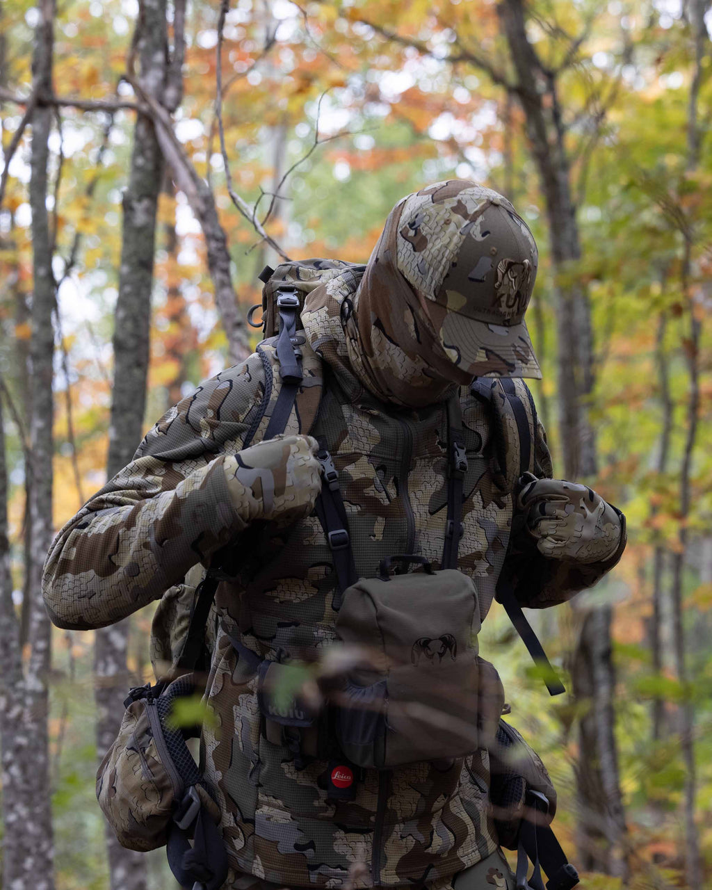 Hunter in the field wearing a Valo Camouflage Hat and the Peloton 240 Full Zip Hoodie in Valo Camouflage adjusting a backpack