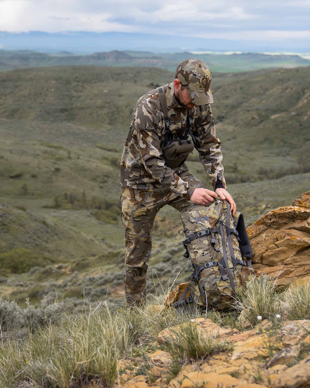 Hunter in the field wearing a full Valo kit including the Peloton 240 Full Zip in Valo Camouflage loading a backpack