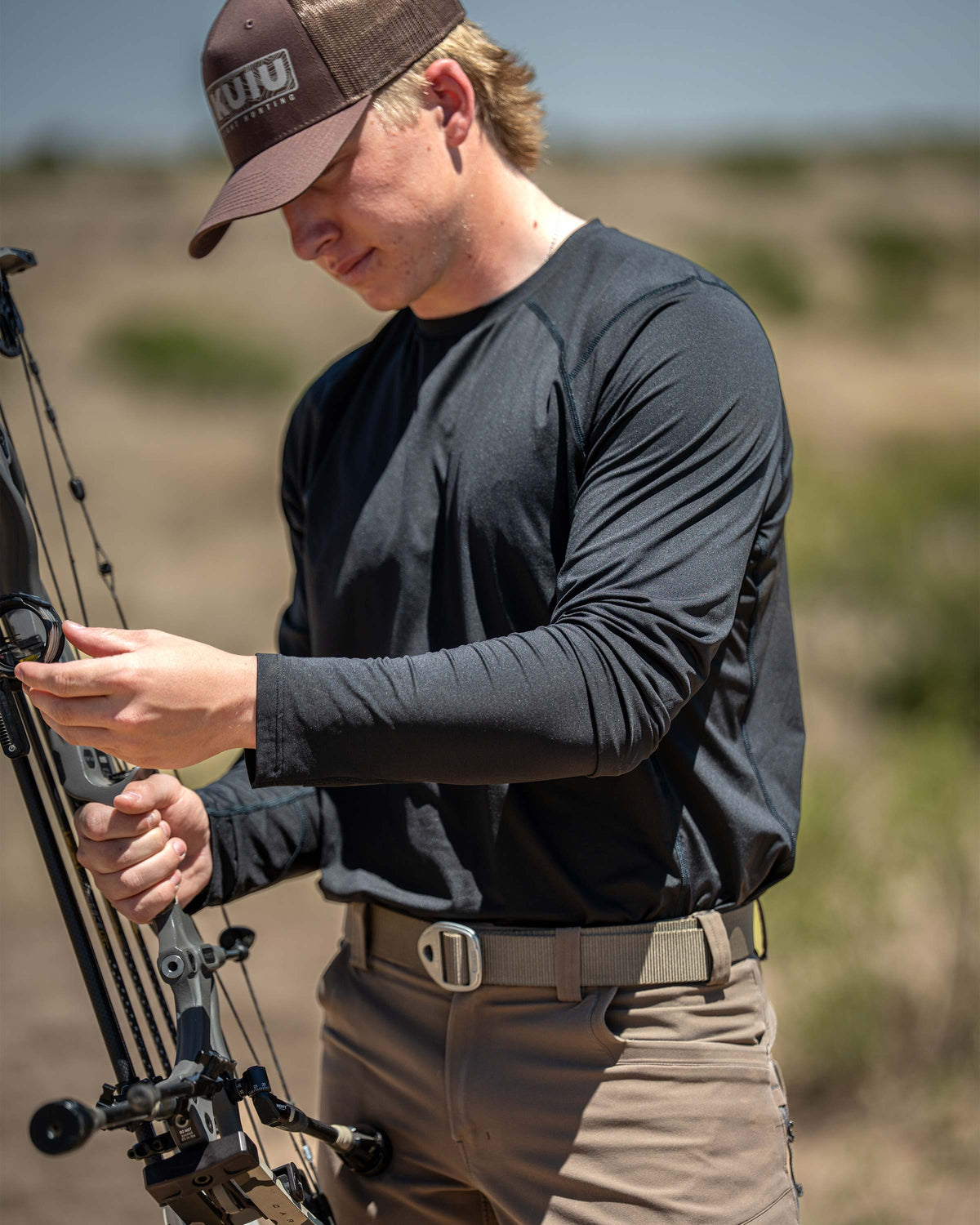 Hunter wearing Vital S2 Long Sleeve Crew in Black, adjusting a compound bow in an outdoor setting.
