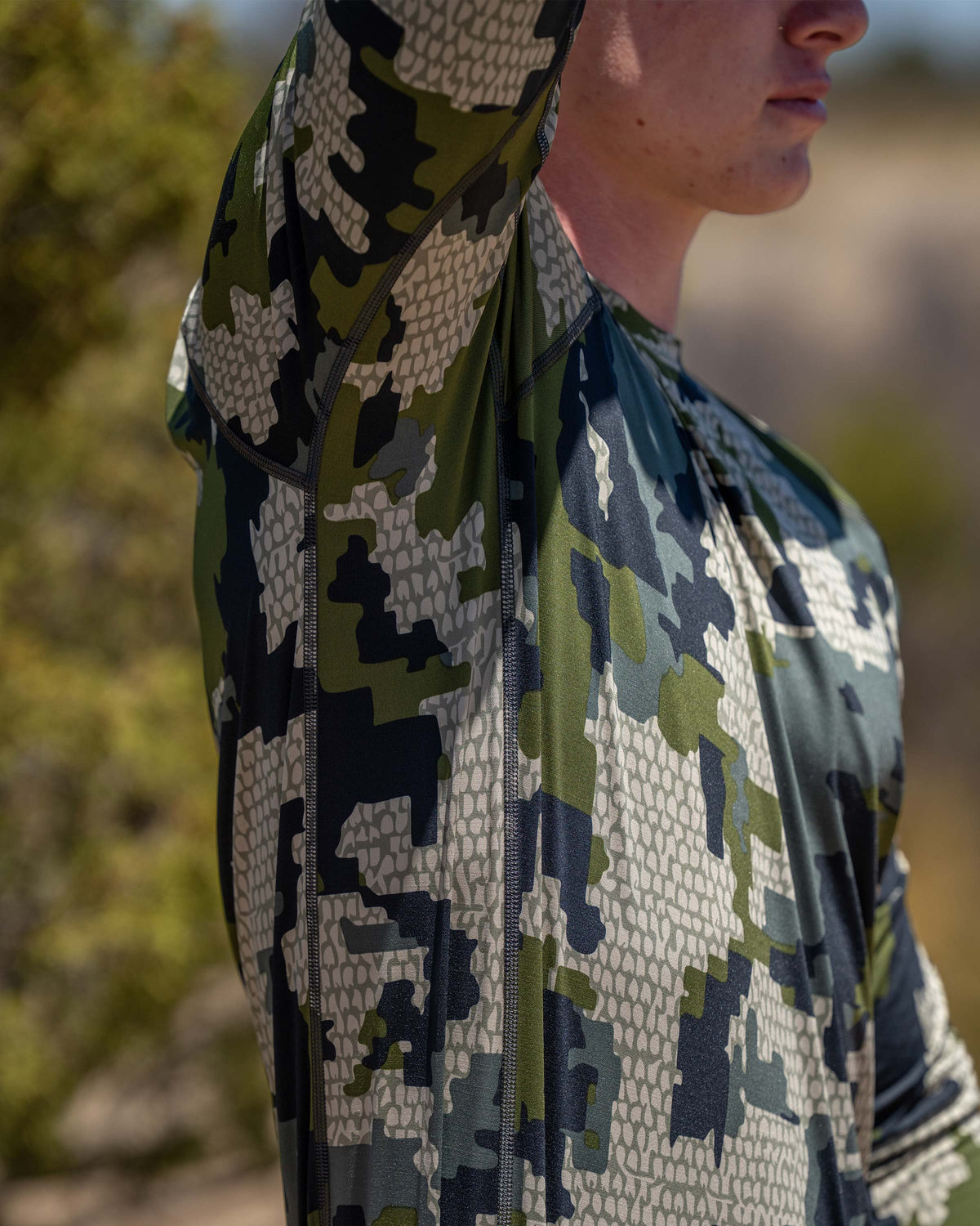 Hunter wearing Vital S2 Long Sleeve Crew in Verde Camouflage demonstrating full shoulder and arm mobility and range of motion when drawing a bow or climbing.