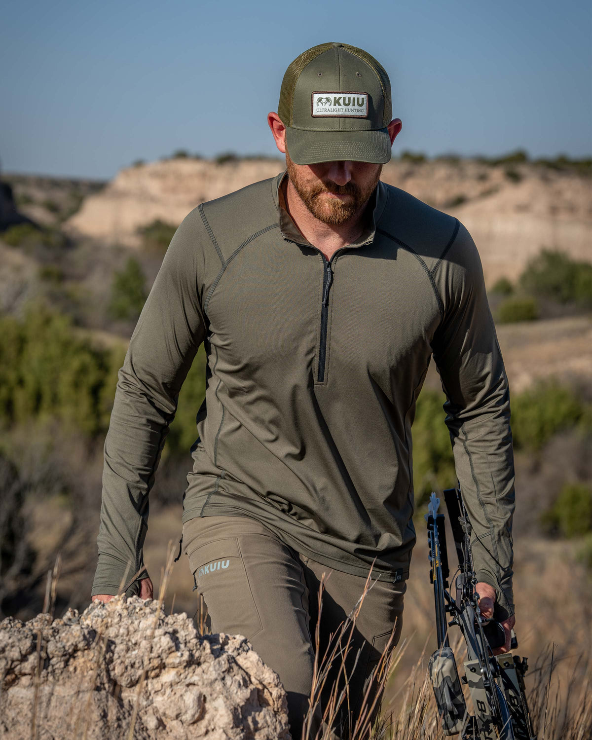 Hunter wearing a Vital S2 Zip-T in Ash Color walking through a low shrubs and rocky foothills.