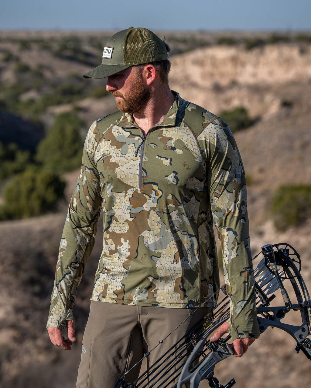 Hunter wearing Vital S2 Zip-T in Valo Camouflage holding a bow in a low shrub desert landscape.