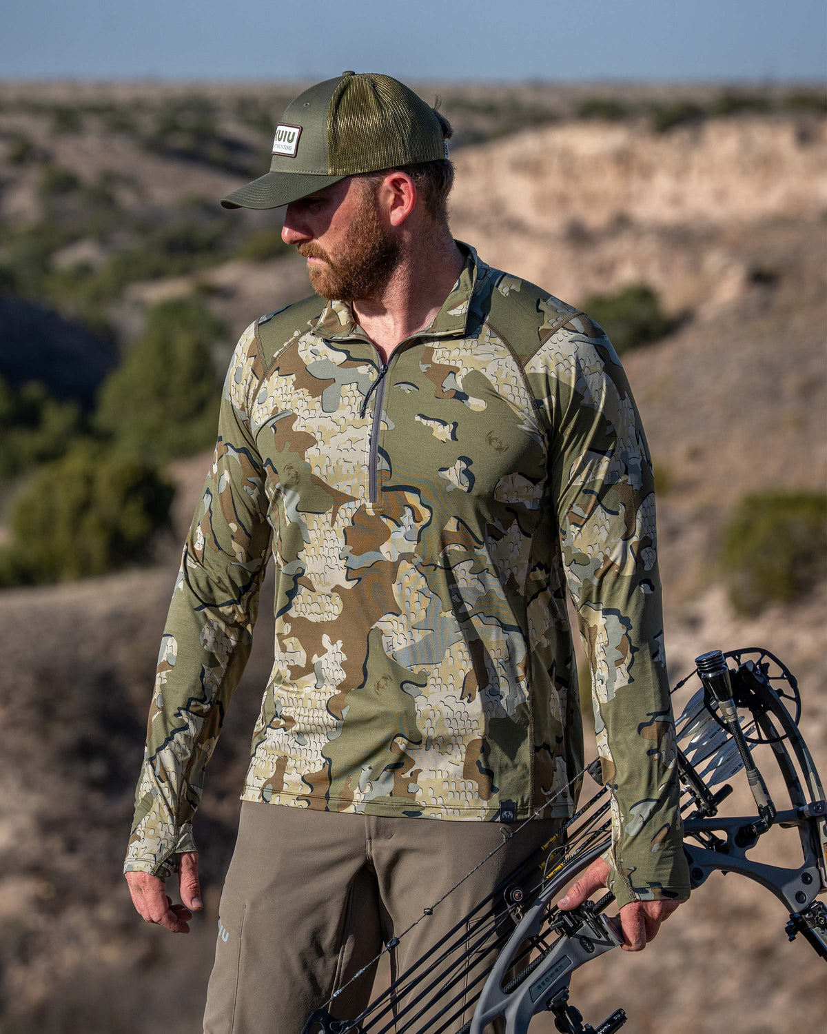 Hunter wearing Vital S2 Zip-T in Valo Camouflage holding a bow in a low shrub desert landscape.