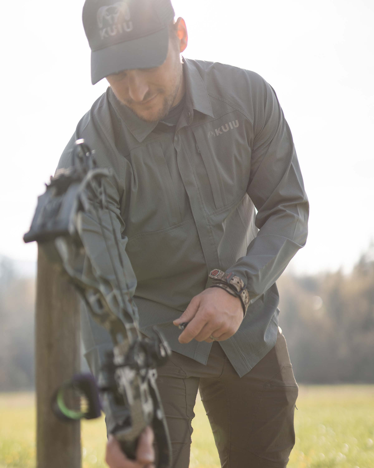 Hunter leaning forward, reaching for his bow, wearing Tiburon Hybrid Snap Shirt in Stone Grey