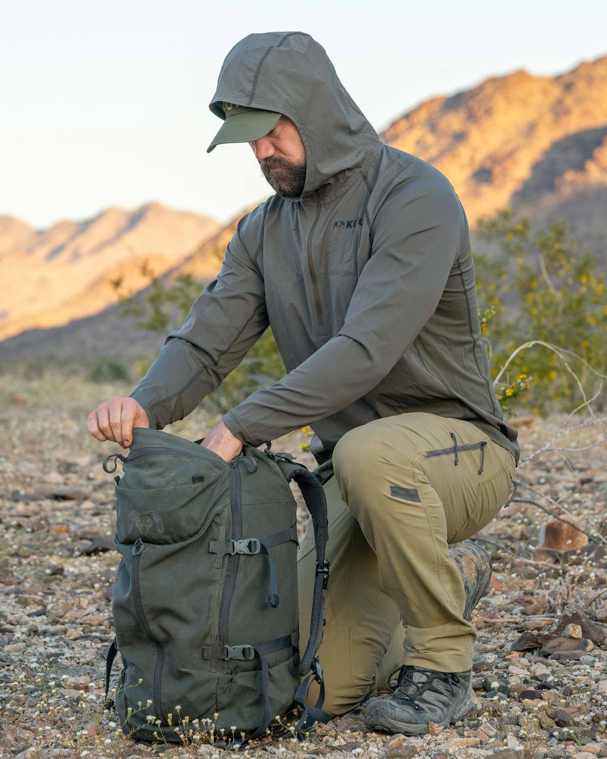 Model kneeled down, reaching in his backpack, wearing Tiburon Hybrid Hoodie in Ash Brown