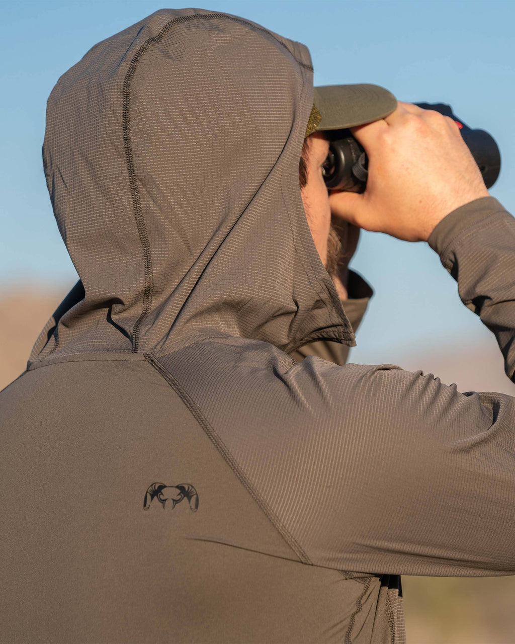 Back of Model wearing Tiburon Hybrid Hoodie in Ash Brown looking through a binocular