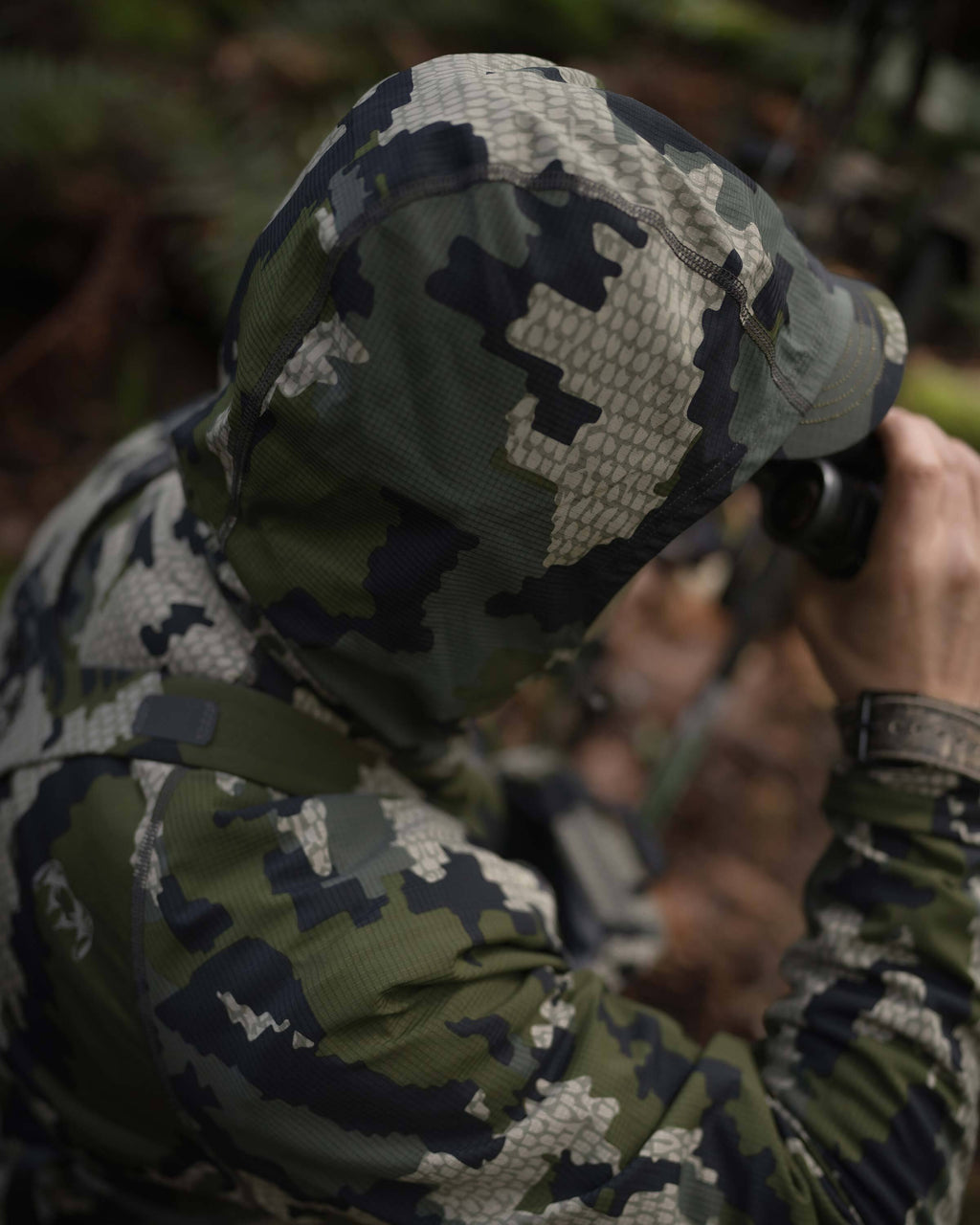 Above head image of hunter glassing with hood over his head, wearing Tiburon Hybrid Hoodie in Verde Camouflage