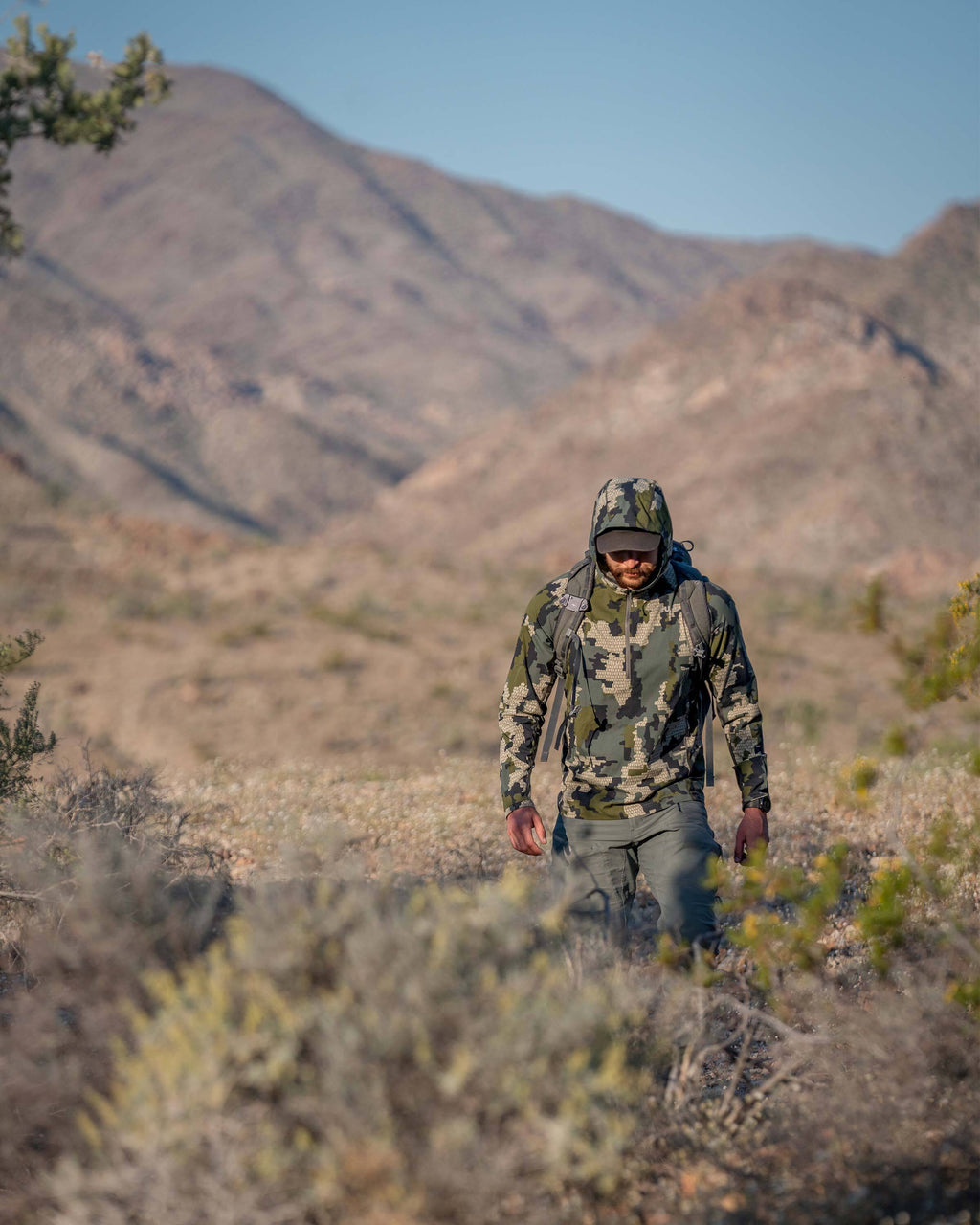 Hunter hiking through a desert terrain, wearing Tiburon Hybrid Hoodie Verde in Camouflage