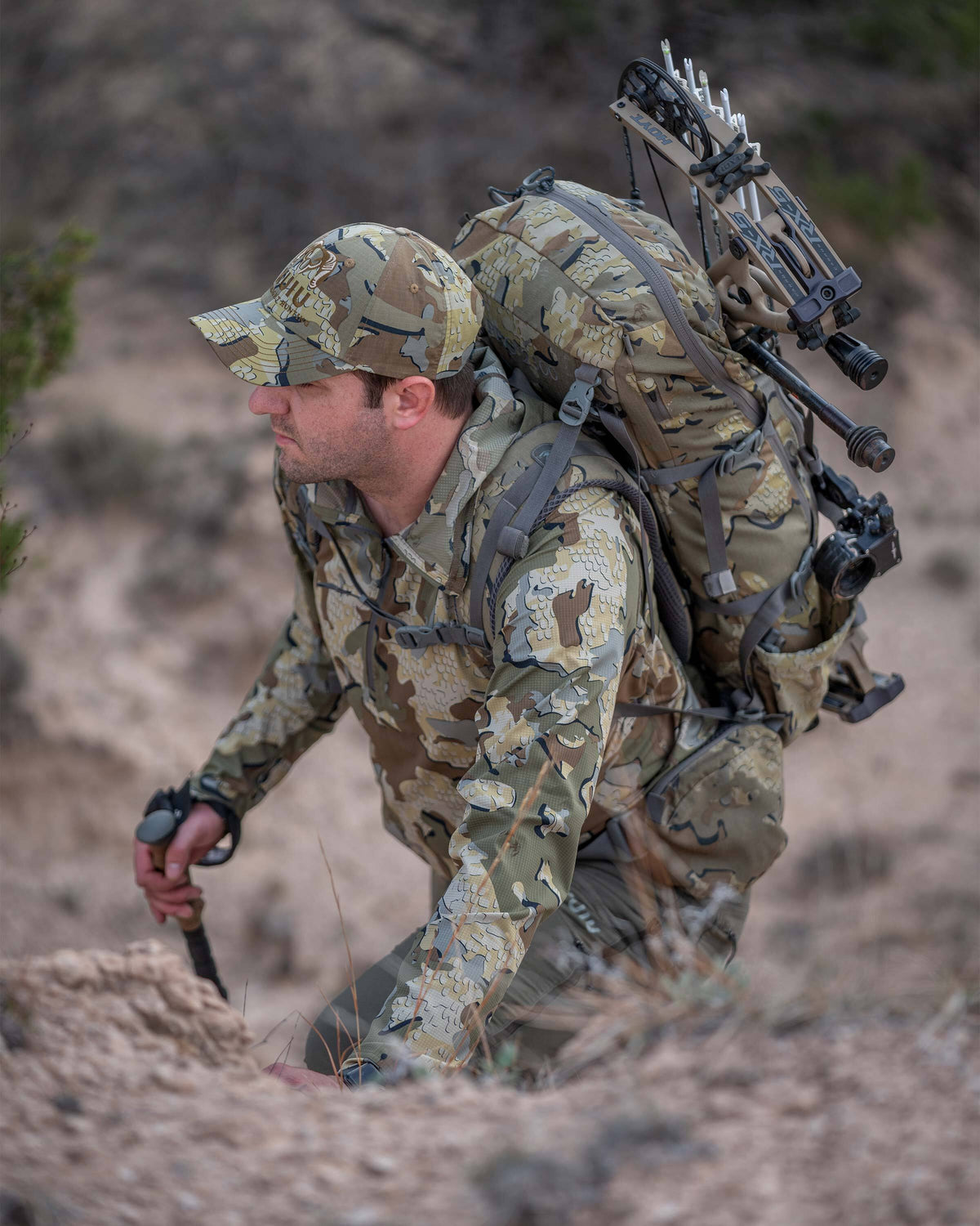 Close-up view of hunter hiking up a rocky hill with a backpack and bow on his back, wearing Tiburon Hybrid Hoodie in Valo Camouflage 