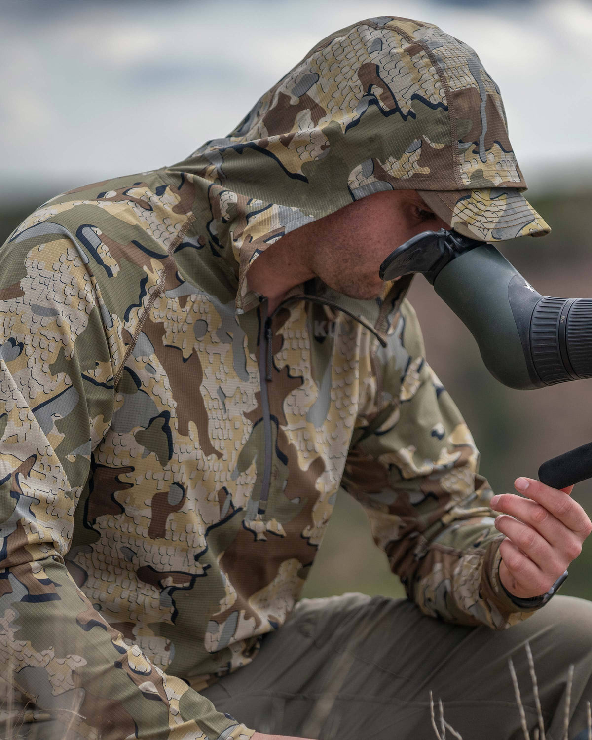 Close-up view of hunter looking through his spotting scope, wearing Tiburon Hybrid Hoodie in Valo