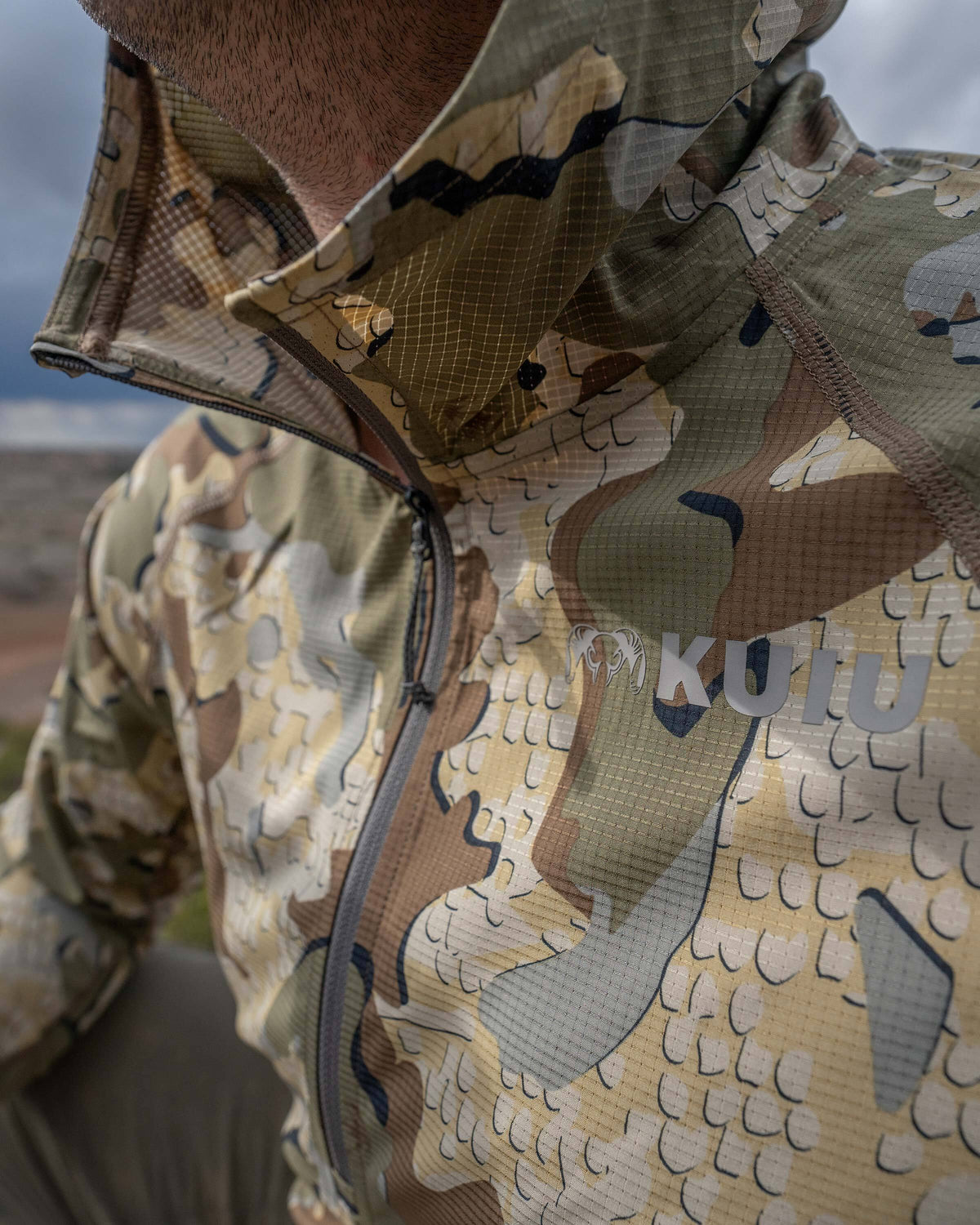 Close-up of hunter's quarter unzipped Tiburon Hybrid Hoodie in Valo Camouflage with visibility of KUIU logo brand