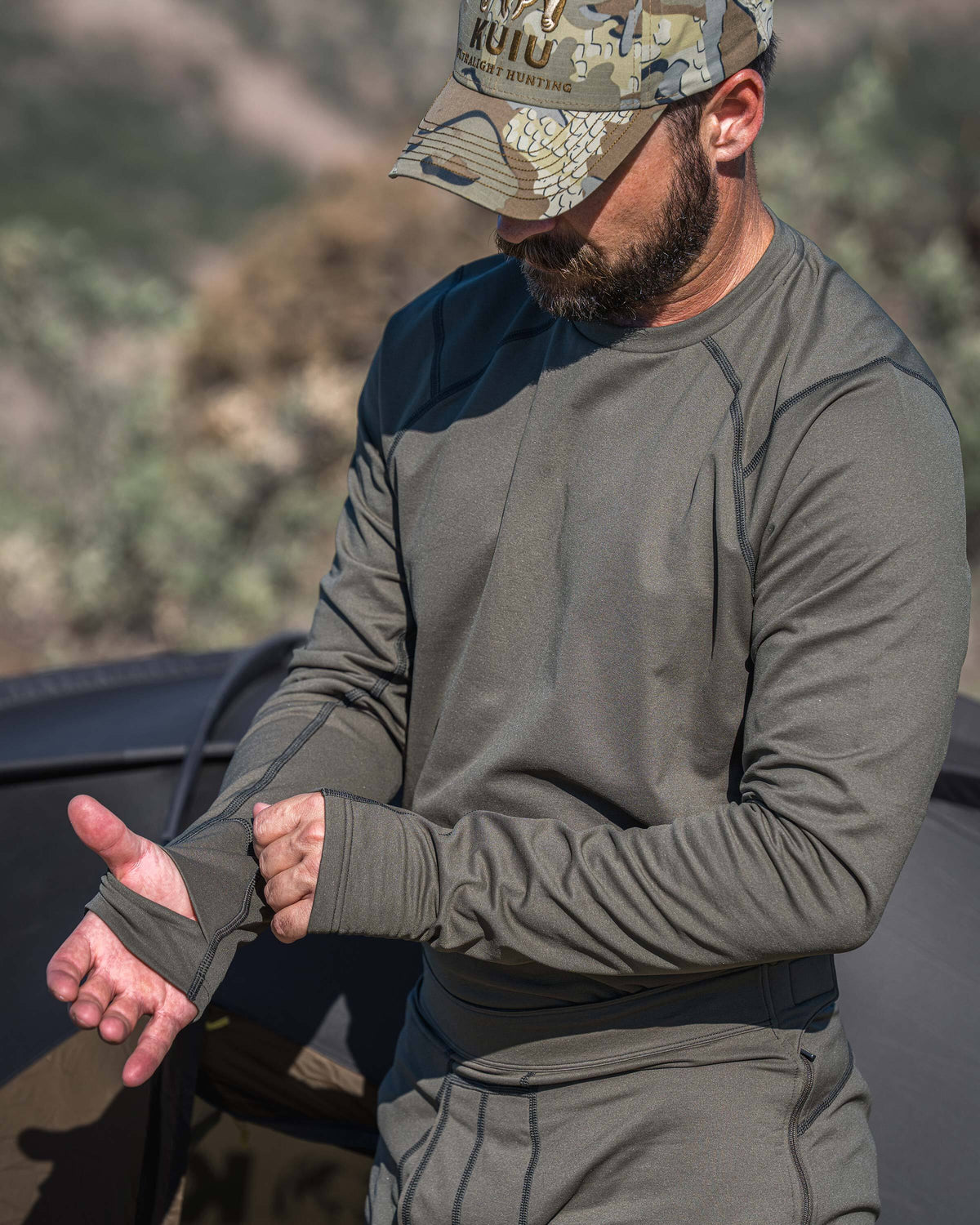 A man outdoors wearing Vital S3 Long Sleeve Crew in Ash Brown, shown adjusting the thumbhole sleeve of the shirt.