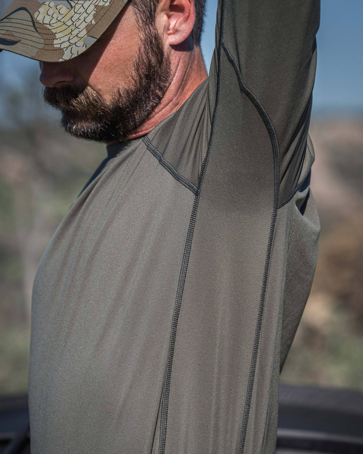 A man wearing Vital S2 Long Sleeve Crew in Ash Color, demonstrating with one arm raised showing full shoulder and arm mobility and range of motion.