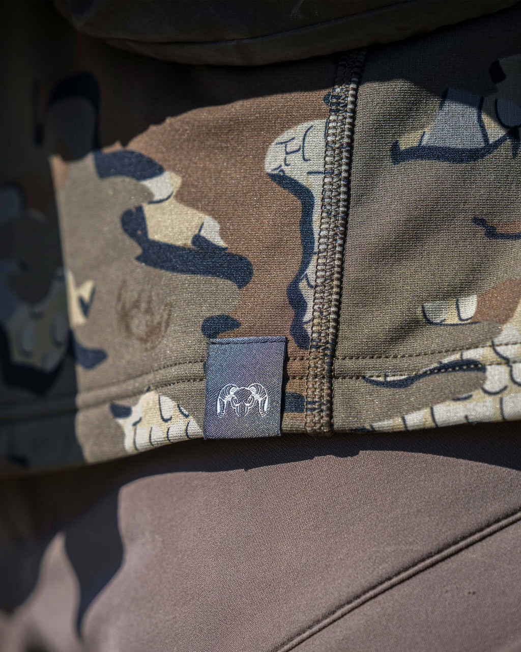 Close-up of bottom seam on the Vital S3 Long Sleeve Crew in Valo Camouflage, displaying a small sewn-in KUIU patch.