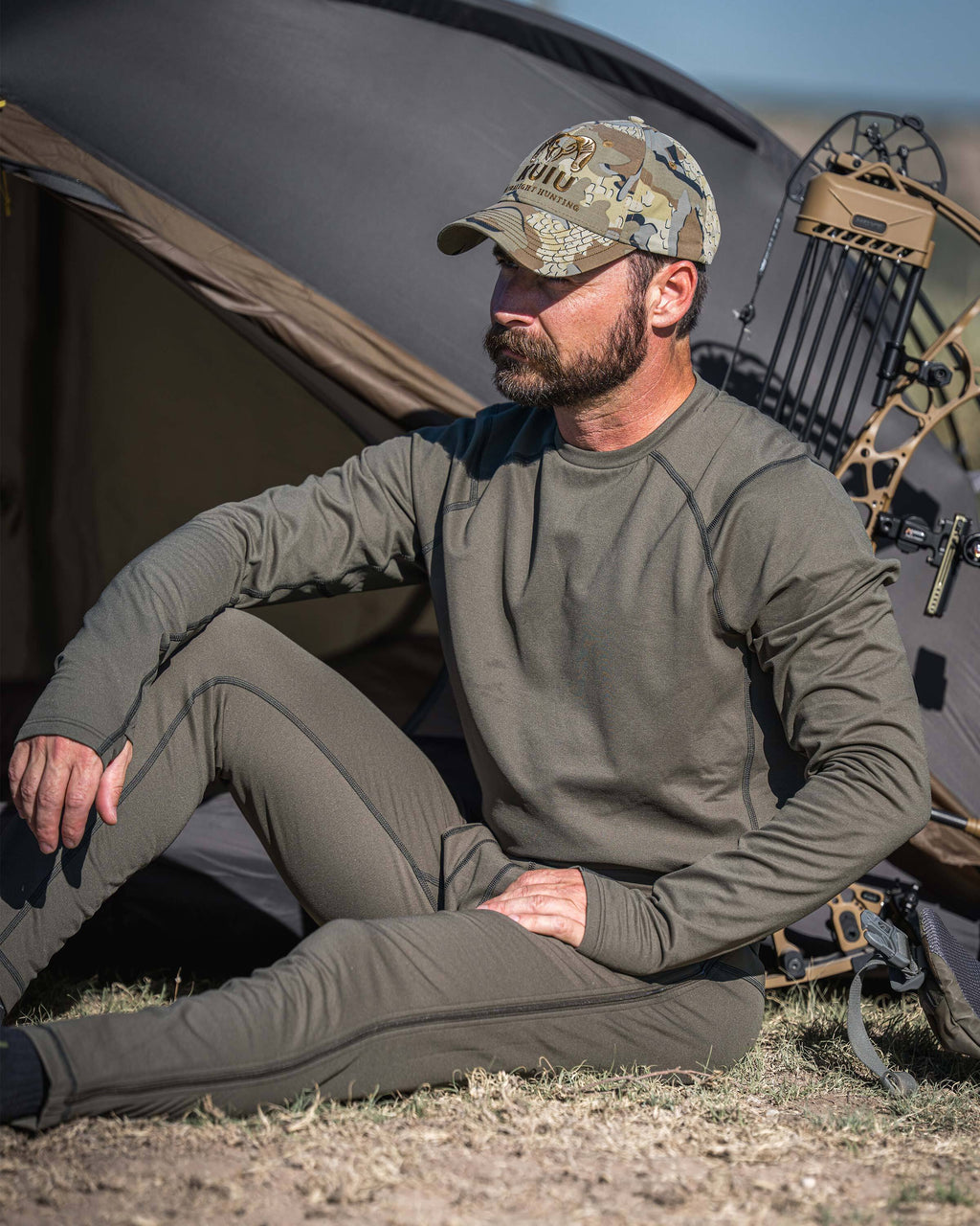 Hunter wearing a Vital S3 Zip-Off Bottom in Ash Brown sits outdoors in front of a tent.