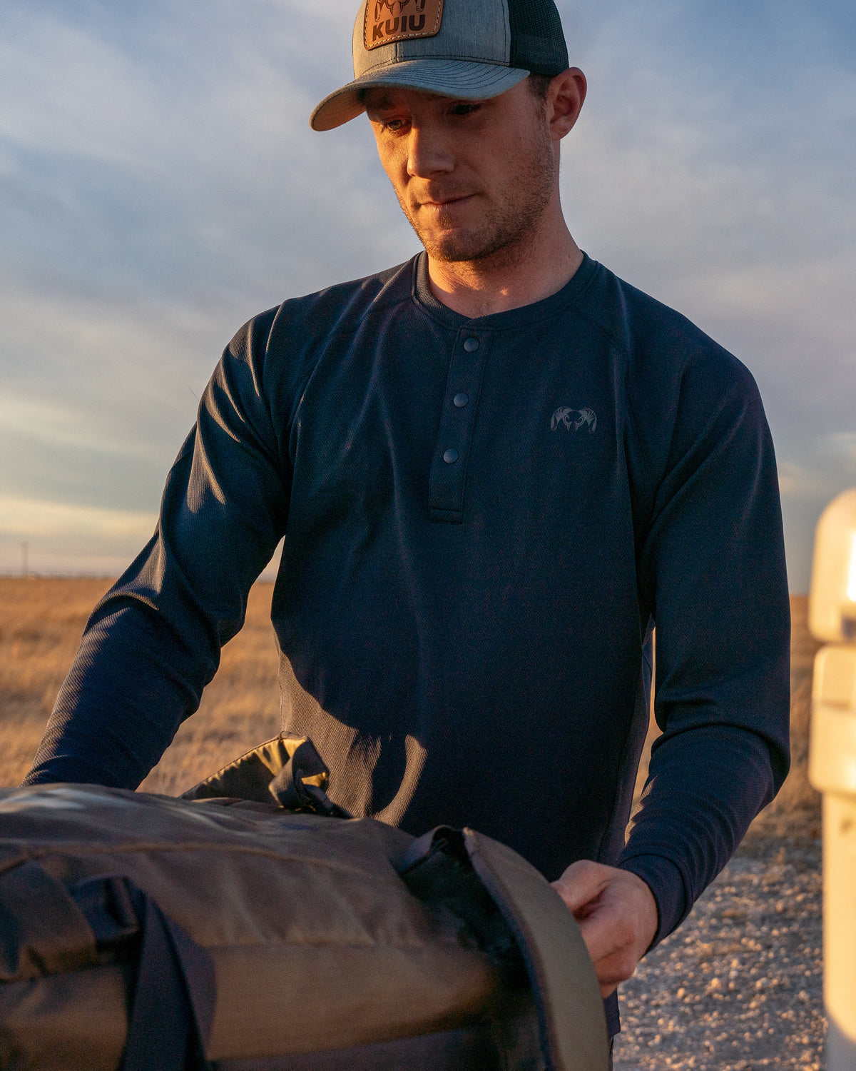 Side of Hunter Loading Waypoint Duffel into Truck Bed Wearing Pro Merino 200 Henley in Steel Blue Color