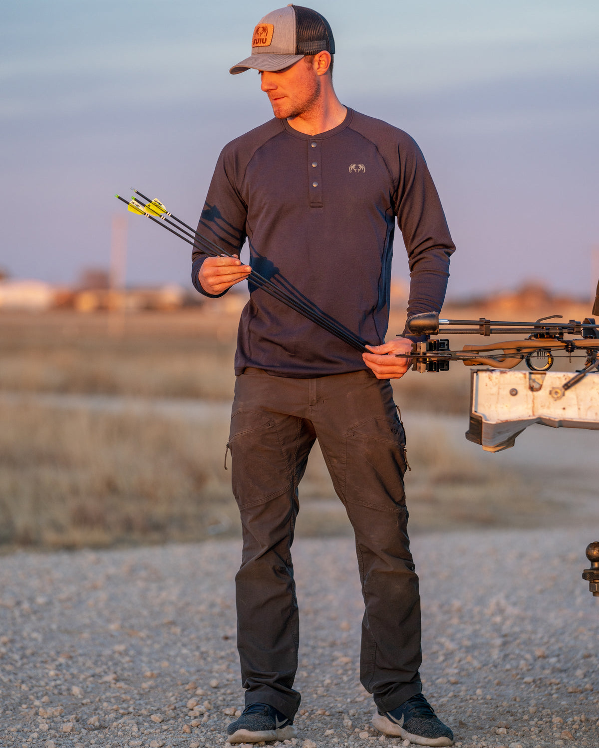 Angled, Front View of Hunter Inspecting Arrows Wearing Pro Merino 200 Henley in Steel Blue Color