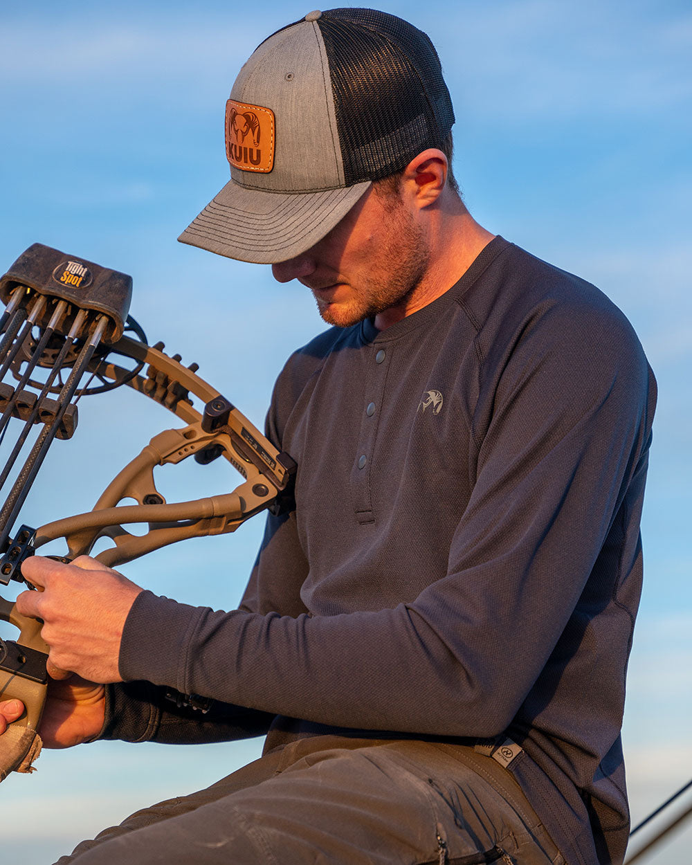 Side of Hunter Holding Bow Wearing Pro Merino 200 Henley in Steel Blue Color