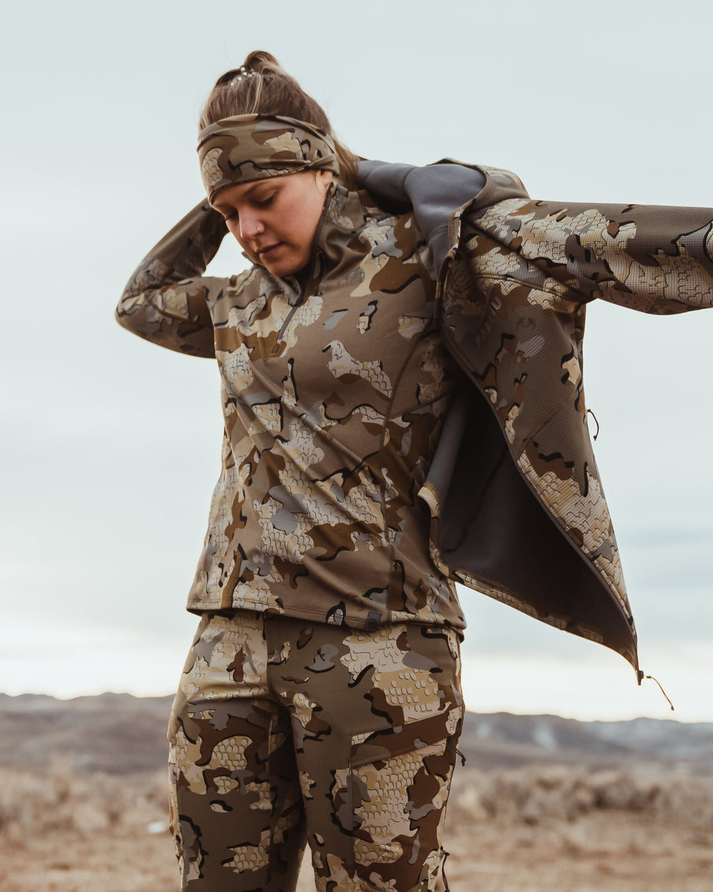 Angled, Front View of Hunter Putting on Peloton 240 Full Zip Hoodie in Valo Camouflage